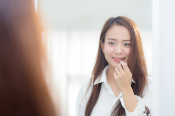 Beauty of portrait of young asian woman at the mirror holding and looking a makeup lipstick, Beautiful girl beauty fashion at the room, lifestyle concept.