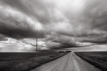 Storm blows through rural Alberta countryside; black and white image of prairie storm with gravel road leading to horizon