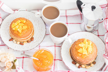 Breakfast for 2. Tray with 2 vintage plates of pancakes with orange jam and nuts and 2 white coffee cups. Top view