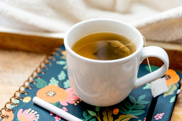 Hot Tea Bag in White Mug on Tray in Bed Blanket Cozy on Floral Notebook Planner Relax In Focus Room for Copy Space