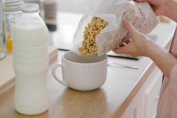 Anonymous young female model preparing cereal with milk for breakfast