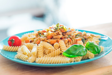 Cooked pasta fusilli with fried mushrooms and vegetables on turquoise plate