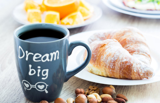Dream big. Good morning breakfast. Mug of coffee with croissants, nuts and oranges
