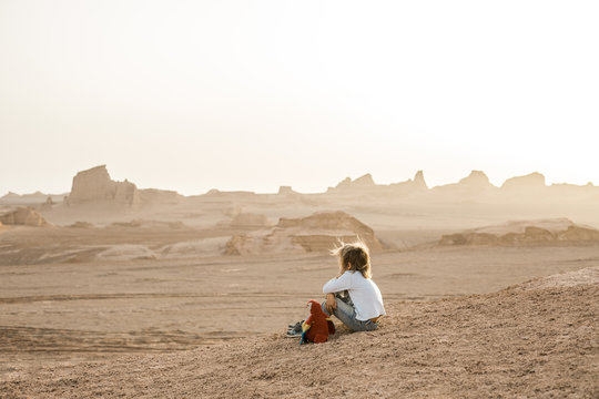 little boy sitting with his parrot in iranian desert landscape enjoying sunset