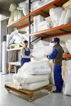 Workers Placing Mattress Packages On Trolley At Sofa Workshop