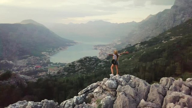 Aerial view of Young traveling woman wearing hat walks on high on the top of the mountain, evening with sunset. Montenegro
