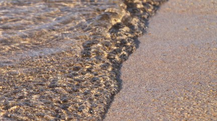 Waves on the sand and water reflecting the grains