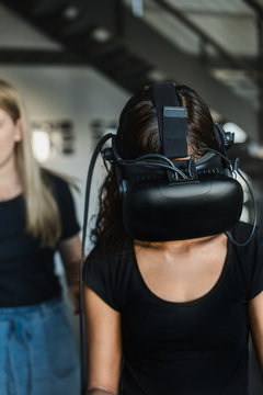 Caucasian young woman helps South-East asian girl putting on VR and controllers