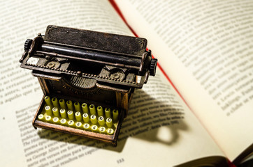 Small typewriter in copper tones in focus on a page of an old book. Decoration item. Concept of...