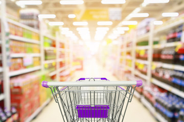 Supermarket aisle product shelves interior blur background with empty shopping cart