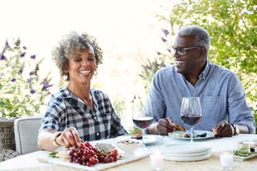 Mature African American couple drinking wine and eating lunch outdoors on the patio at home