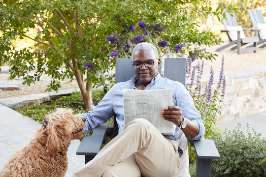 Portrait of African American Senior man reading the newspaper on his patio outside with his dog
