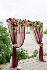 Beautiful wedding arch decorated with cloth and flowers on the beach of river or lake outdoors, copy space. Wedding setup. Place for wedding ceremony in open air