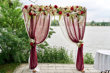 Beautiful wedding arch decorated with cloth and flowers on the beach of river or lake outdoors, copy space. Wedding setup. Place for wedding ceremony in open air