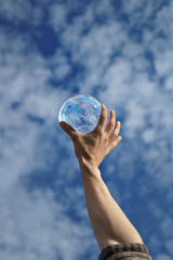 Contact juggling. Hand and acrylic ball against sky. Cumulus clouds are reflected in sphere