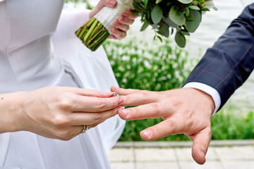 Bride putting wedding ring on groom's finger at wedding ceremony outdoors, close up.