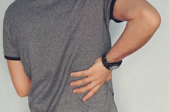 Close Up Of A Man Holding His Back In Pain. Sick Kidney. Pain In The Kidneys. Renal Failure. Patient Holds His Hand Behind His Back. Arthrosis, Chondrosis, Osteoporosis, Muscle And Joint Pain