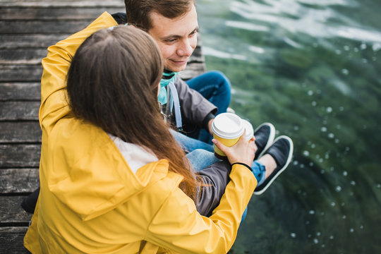 Couple in raincoats sitting on the peer of the lake