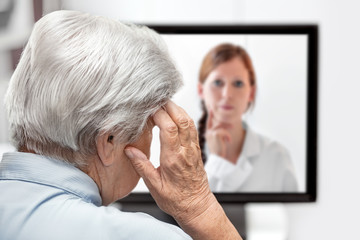 Seniorin mit Kopfschmerzen, Ärztin auf dem Monitor, Telemedizin und Fernbehandlung