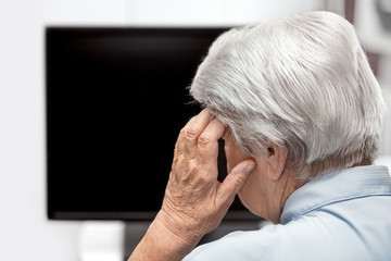 Seniorin sitzt vor Monitor oder Fernseher und hat Kopfschmerzen, Überforderung und Stress