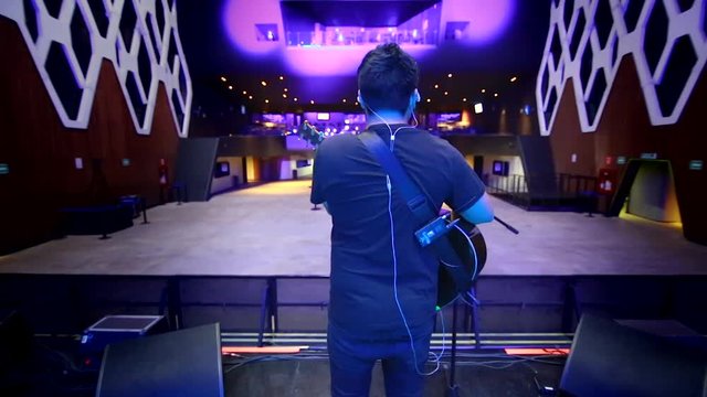 Singer playing acoustic guitar during sound check in front of empty auditorium