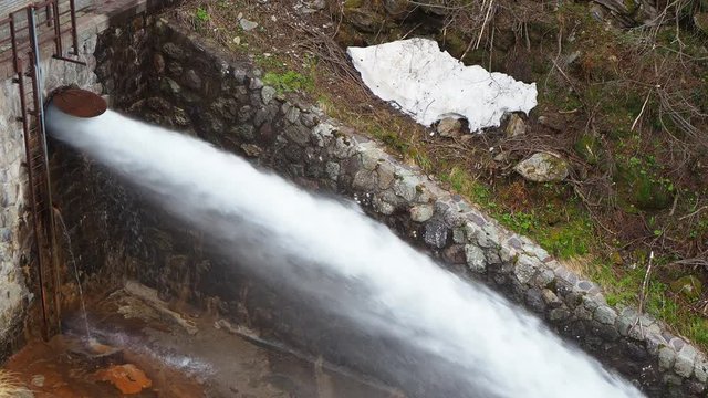Water discharge from the dam of the Lake Fregabolgia an Alpine artificial lake. Italian Alps. Italy. The water flows rapidly and splashes onto the ground