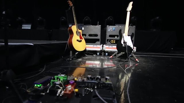 Acoustic & Electric guitars on stands on a stage with guitar amp & lighting rig