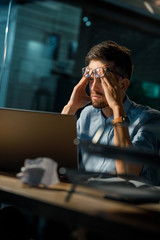 Casual man in glasses looking super exhausted and rubbing forehead while sitting at table with...