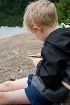 Young Boy Sharpening a Stick With a Knife While on Backcountry Wilderness Camping Canoe Trip