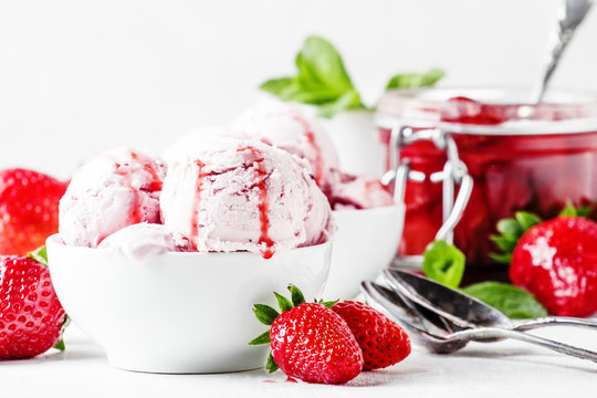 Strawberry ice cream with jam topping, decorated with green mint leaves, gray background, selective focus
