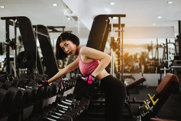 Naklejka na ściany i meble Attractive fit woman workout with dumbbell in gym fitness. Portrait sport and Healthy concept.