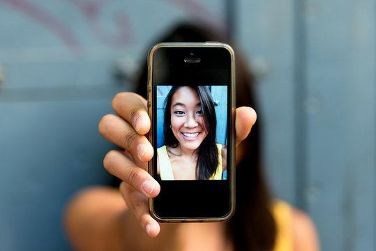 Asiatic woman smiling and taking a selfie with her smartphone