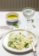 Gentle cream risotto with spinach, served with wine. Light background.