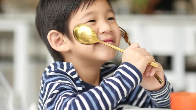 Cute Asian child holding a spoon and fork with empty white plate  in restaurant 