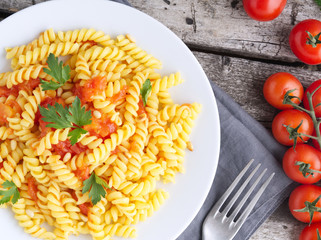 Pasta fusilli with tomatoes with parsley on a old rustic gray wooden background, low-calorie diet, top view, close-up