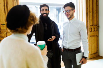 Cheerful businessmen talking to businesswoman during lunchbreak in office.
