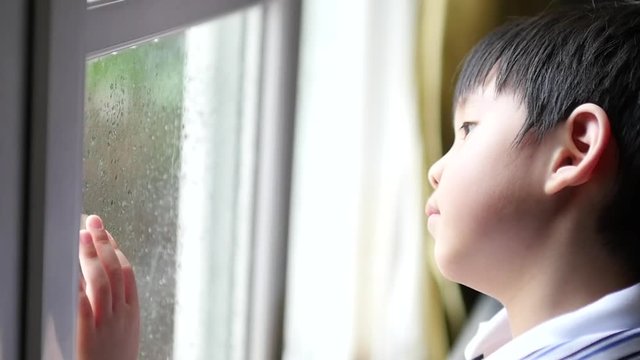 Cute Asian child looking out through the window with the rain 