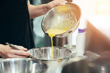Asian women are mixing the sugar and eggs ingredients of a cake in a stainless bowl in her kitchen for weekend party.