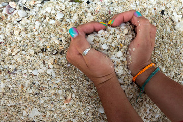 the girl's hands with a beautiful manicure, with ring on her finger and baubles (fandangle, Sequin bracelet, friendship bracelets) on her wrist keeps the sand from the shells in the shape of heart