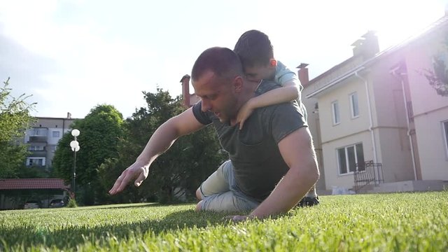 Family fun on backyard, father push-ups from grass physical education for kid son on his back falling on grass