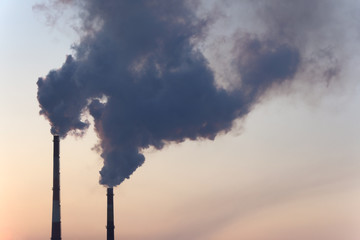 Smoke from two industrial chimneys (pipes) against the orange - blue sky. Global warming. Air pollution.