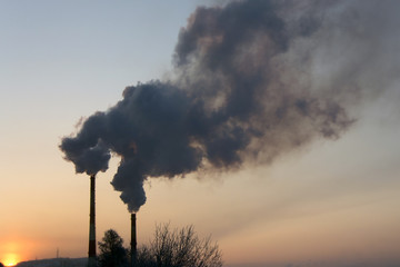 Smoke from two industrial chimneys (pipes) against the orange - blue sky. Global warming. Air pollution.