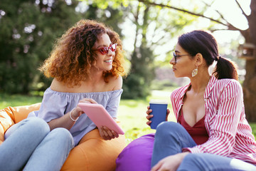 My best friends. Happy curly-haired woman holding a tablet and talking with her friend