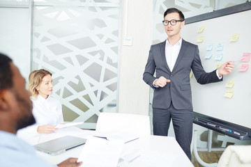 Businessman in glasses and elegant suit talking to colleagues in white modern office with decorations