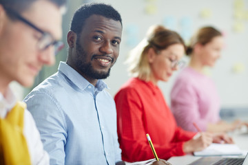 Office worker in casual clothes sitting at job with people in colore shirts on background