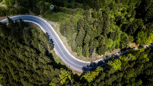 Beautiful aerial view of dense forest mountain landscape in summer time with curvy road cutting through forest. Aerial view by drone . Romania