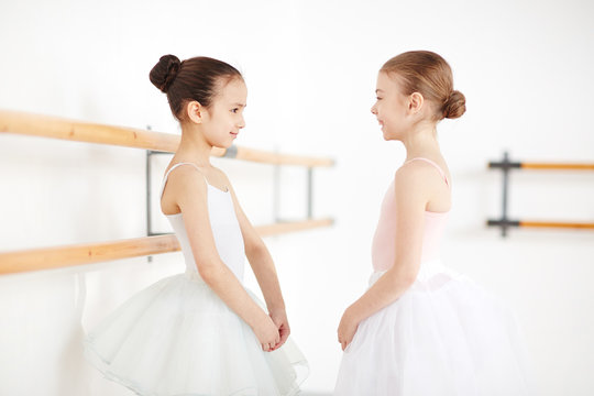Young ballerinas with strict hairstyle staying and smiling in white room with sunlight