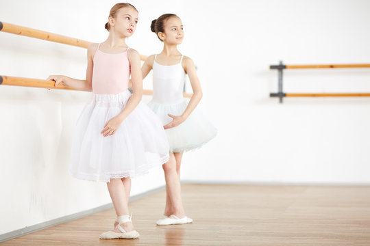 Little ballerinas making position in white clothes at wooden machine in school