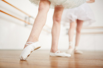 Faceless girls leg in ballet shoes making position on parquet with ballerina on background