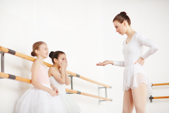 Young girls in white tutu listening pedagogue in short dress with emotions in light dancing studio